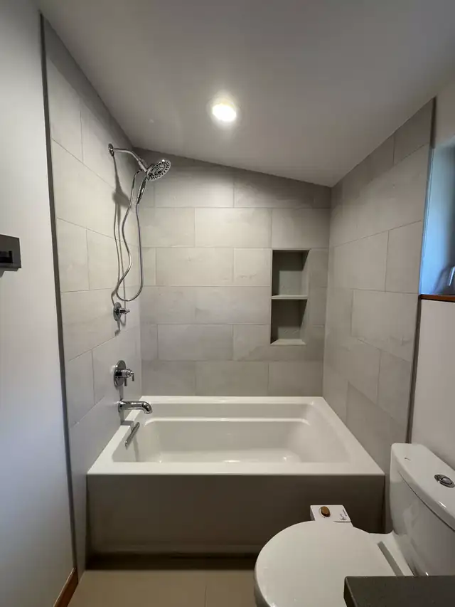 Gray porcelain tub and shower combination with a recessed niche and chrome handheld shower