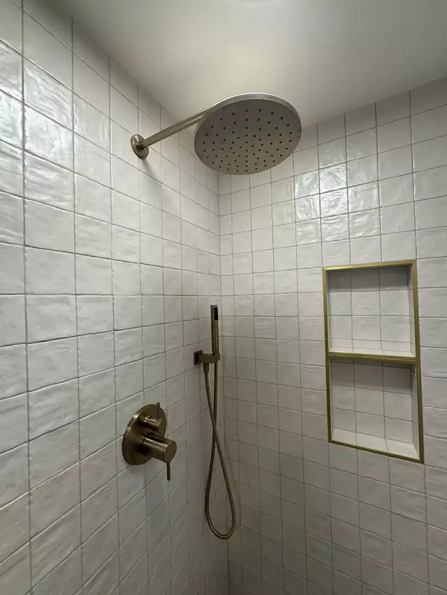 Shower wall in white handmade-look square tile with a brass rain head and brass-trimmed niche