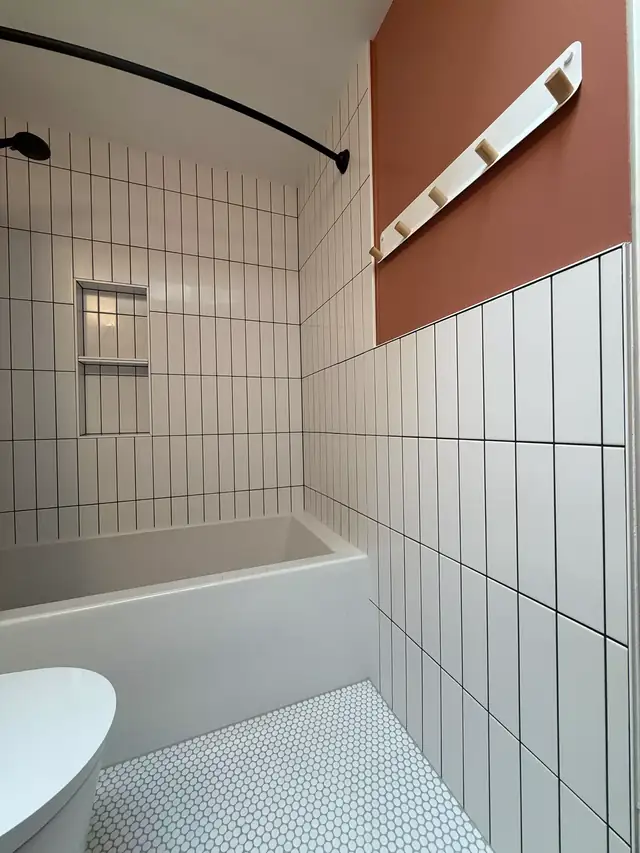 Bathroom with white vertical stacked tile, white penny tile floor, terracotta accent wall and soaking tub