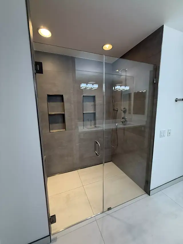 Walk-in shower with a frameless glass door, large gray wall tile and two built-in niches