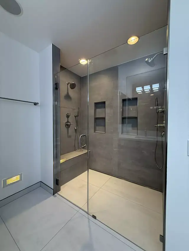 Gray tile walk-in shower with a built-in bench, twin wall niches and a frameless glass enclosure