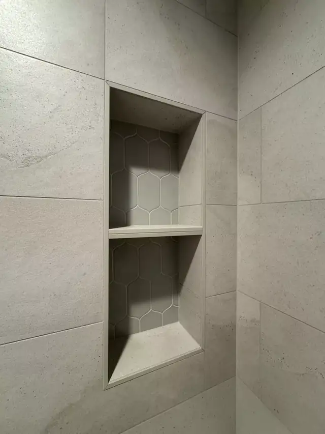Shower niche with two shelves set into large-format stone-look tile with a hexagon tile back