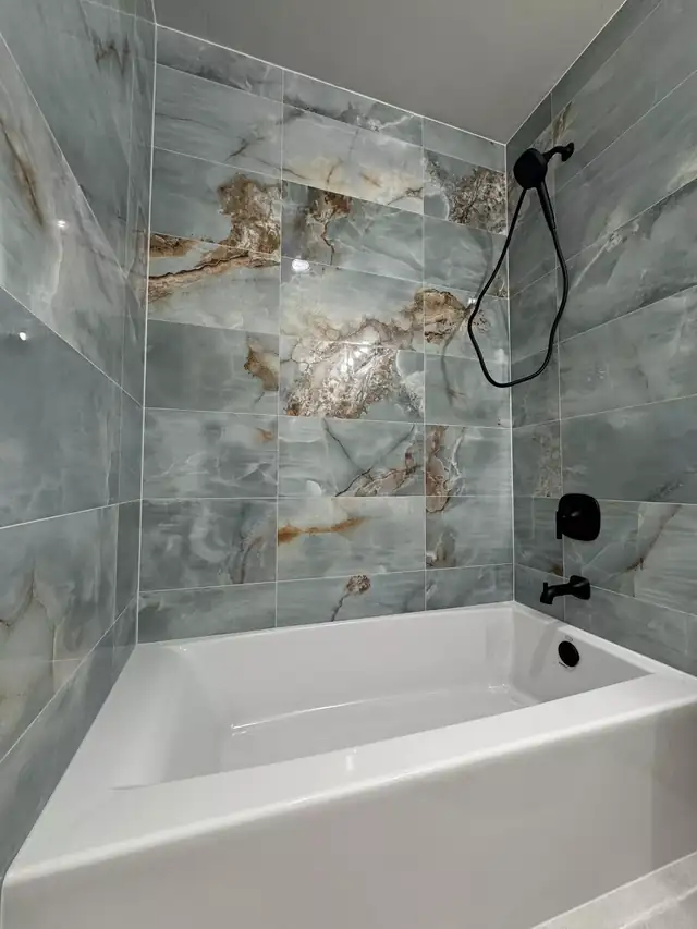 Tub surround in large blue and gold marble-look porcelain tile with matte black shower fixtures