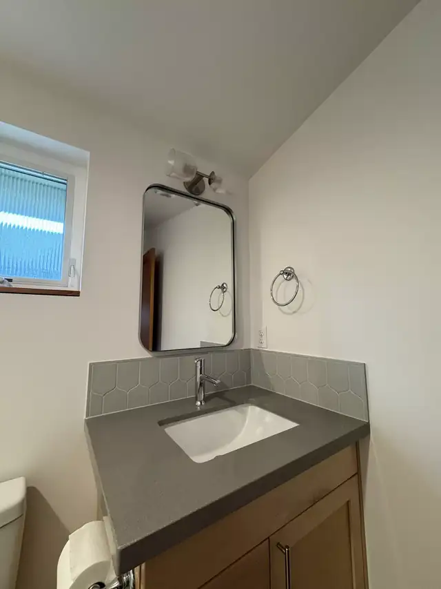 Corner vanity with gray quartz top, undermount sink and black-framed mirror
