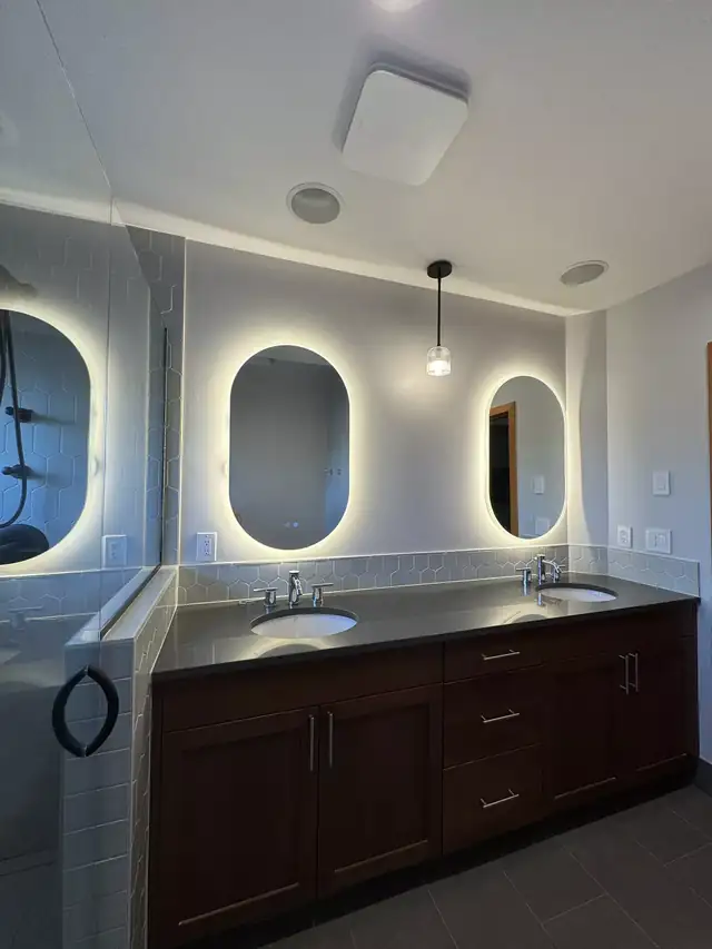 Bathroom with a dark wood double vanity, two undermount sinks and backlit oval mirrors