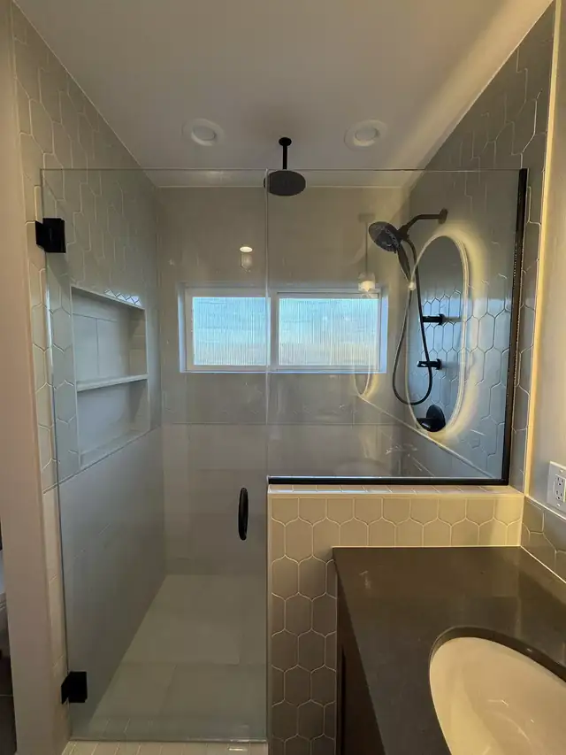 Walk-in shower by Remont with a glass panel, hexagon wall tile, a niche and a backlit mirror over the vanity